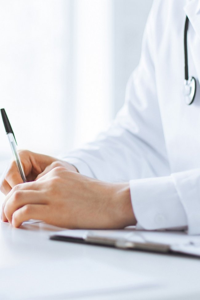 Arzt unterschreibt, Patient sitzt daneben.