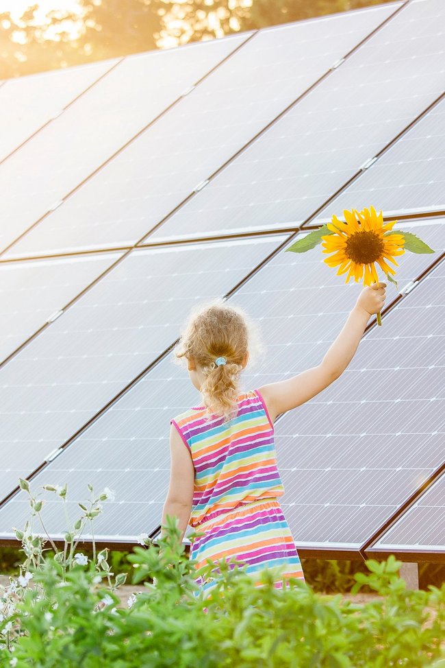 Kleines Mädchen mit Sonnenblume vor PV-Anlage